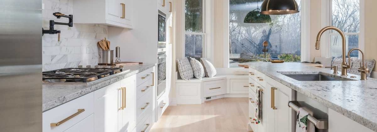 Modern kitchen remodel featuring white cabinetry, gold hardware, marble countertops, and a spacious island with updated fixtures and lighting.