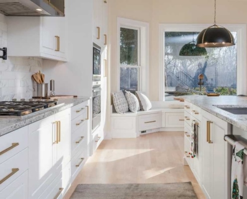 Modern kitchen remodel featuring white cabinetry, gold hardware, marble countertops, and a spacious island with updated fixtures and lighting.