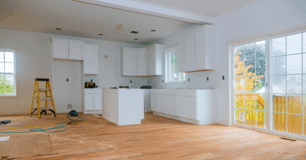 Boise kitchen under renovation in fall with new white cabinetry, hardwood floors, and large sliding glass doors overlooking autumn foliage.