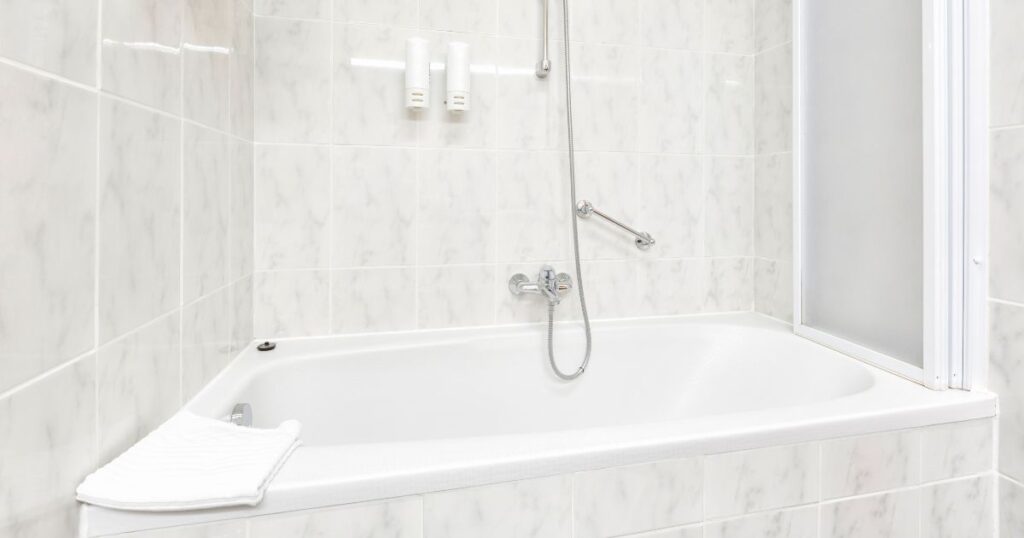 White acrylic bathtub and shower combo with marble-patterned wall panels and chrome fixtures, typical of Bath Fitter-style installations.